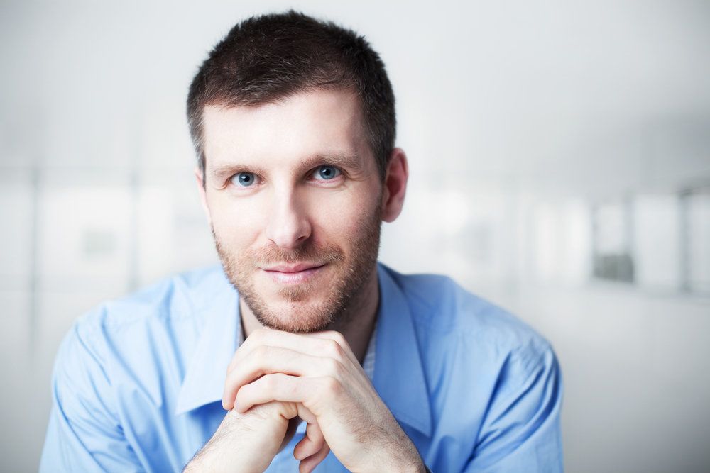 Smiling man with very blue eyes holding hands under chin